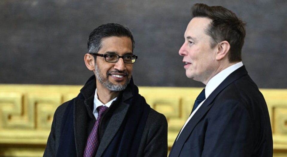 Two men in business attire converse indoors, one wearing glasses and a scarf against an ornate gold background.