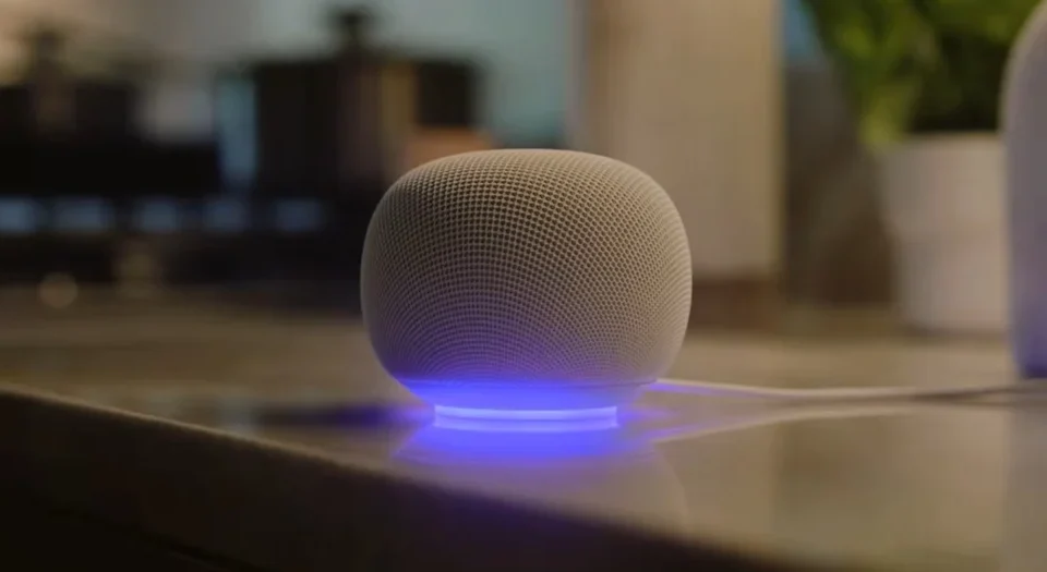 Round smart speaker with fabric mesh, resting on a base with a blue LED glow on a table.
