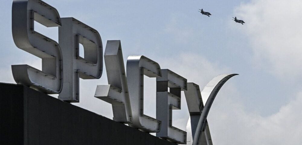 Article Image - Best AI Tools Close-up of a large metallic rooftop sign with bold letters, with two small planes flying in the sky.
