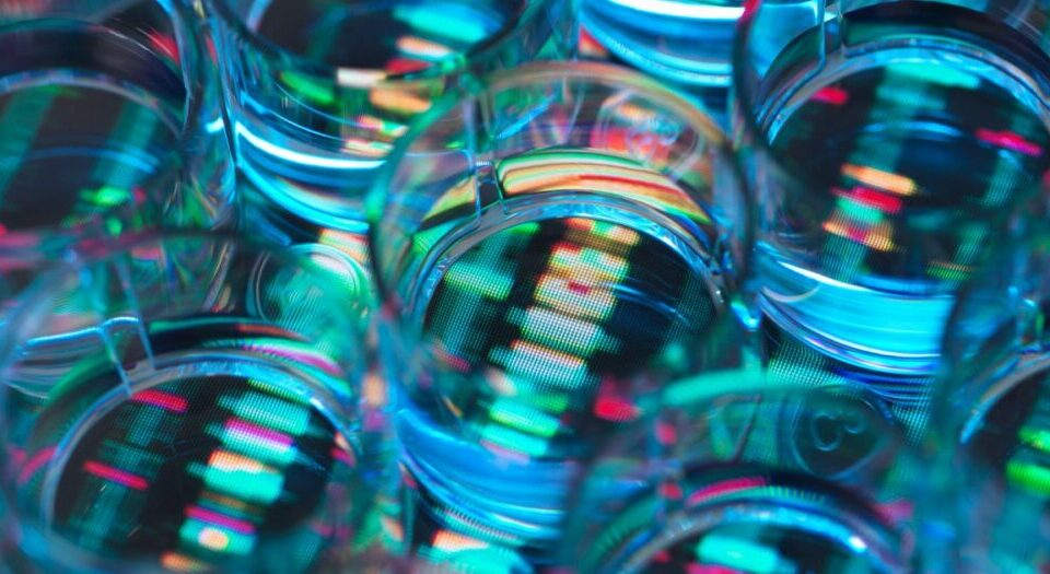 Article Image - Best AI Tools Close-up of stacked glass cups with neon-blue reflections and a digital stock ticker visible through the glass.
