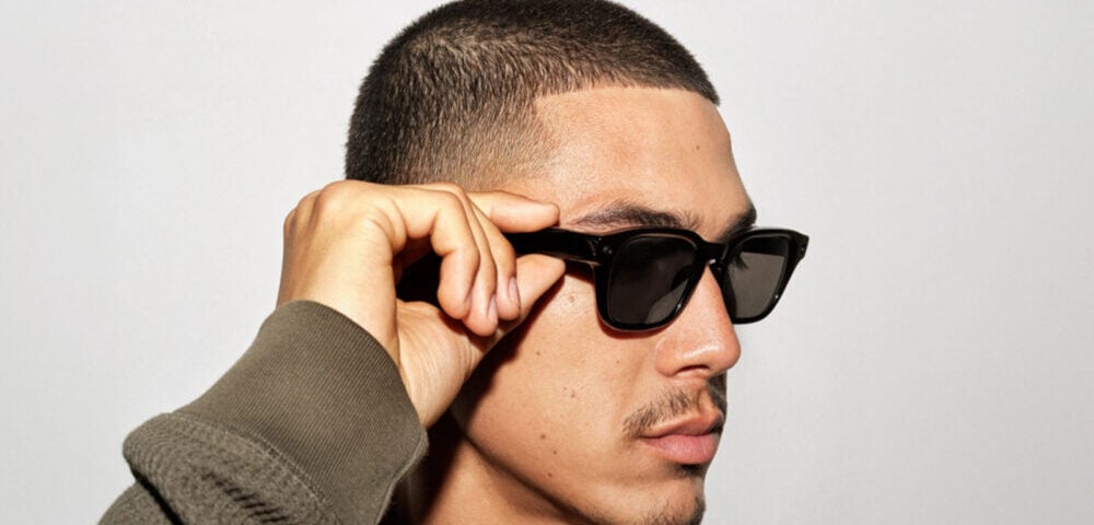 Article Image - Best AI Tools Man with short hair adjusting black sunglasses, facing left against a light background.