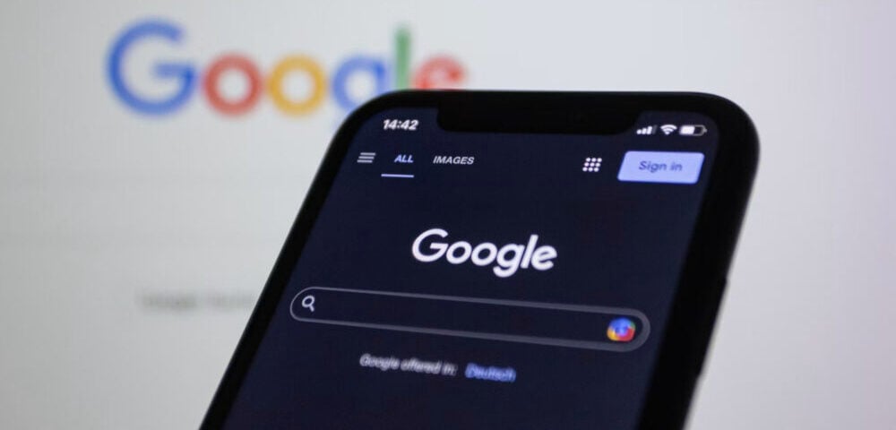 Article Image - Best AI Tools Smartphone screen showing the Google search page in dark mode, with a blurred colorful Google logo in the background.