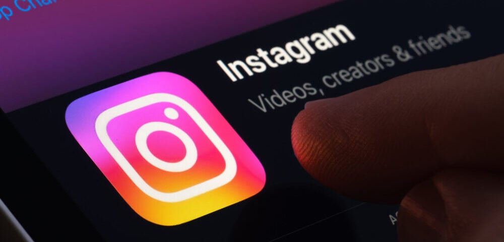 Article Image - Best AI Tools Close-up of the Instagram app icon on a smartphone screen, with a finger nearby and the text 'Instagram' and 'Videos, creators & friends'.