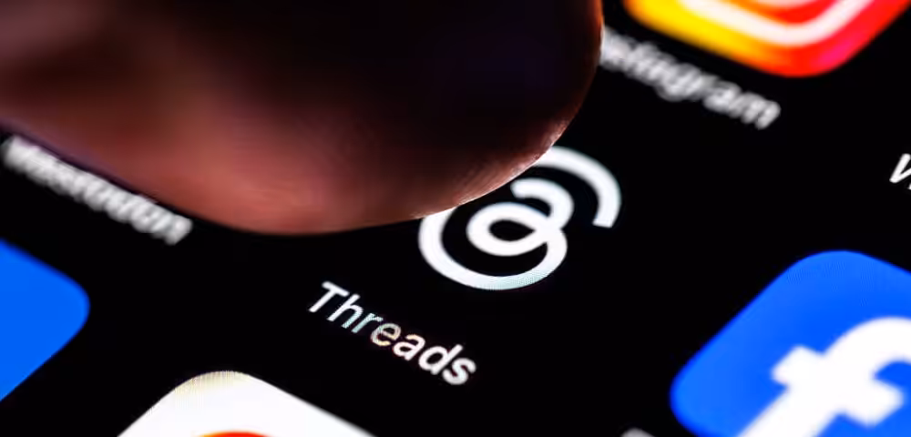 Close-up of a finger tapping near the Threads app icon on a smartphone screen.