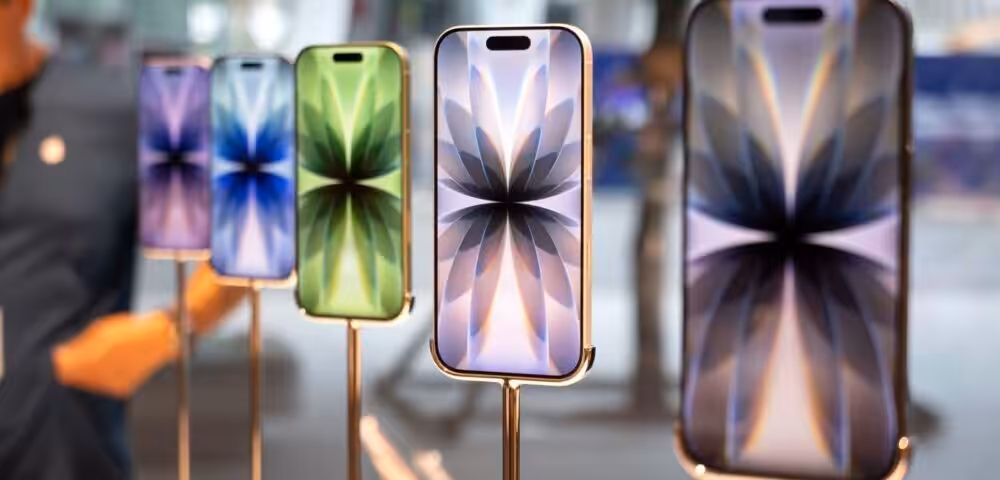 Several iPhones on display stands in a store, showcasing different colors and gold frames with patterned screens like flower petals behind glass.