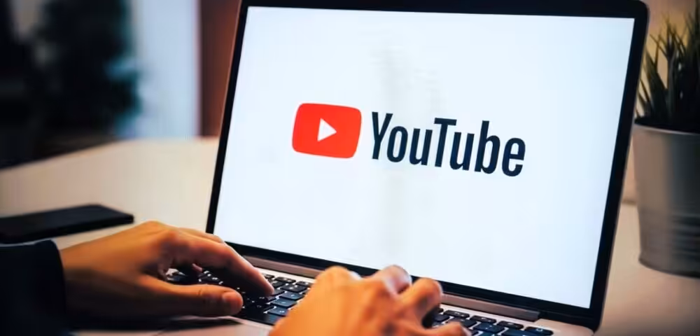Person typing on a laptop with the YouTube logo displayed on the screen.